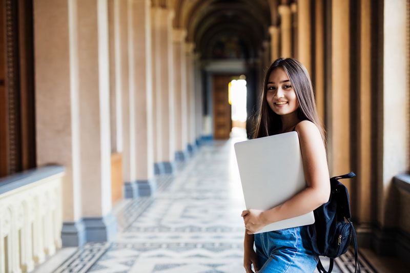 girl college student standing in a university hallway holding a laptop